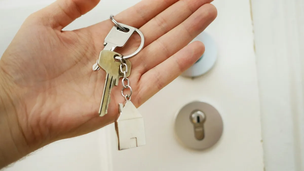 Hand holding house keys with key tag in front of door