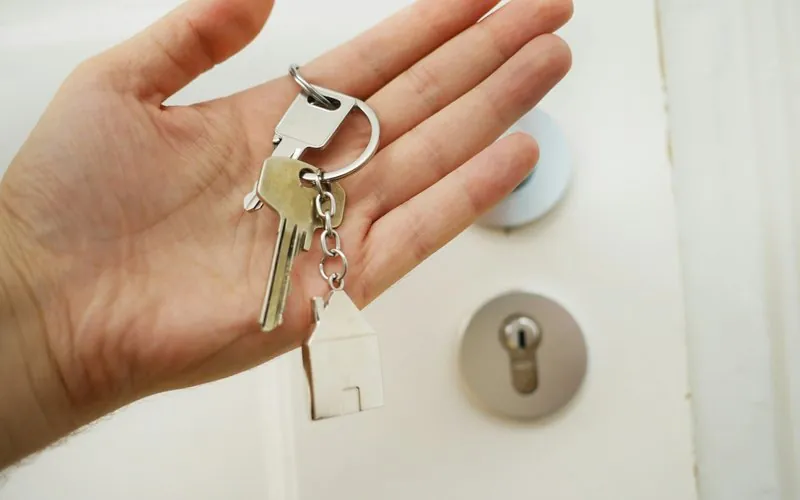Hand holding house keys with key tag in front of door